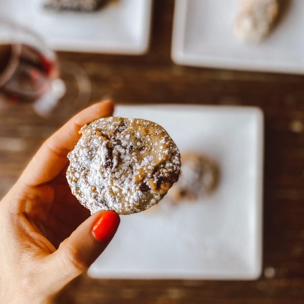 A hand with red nail polish holds a powdered sugar-dusted cookie above white plates.