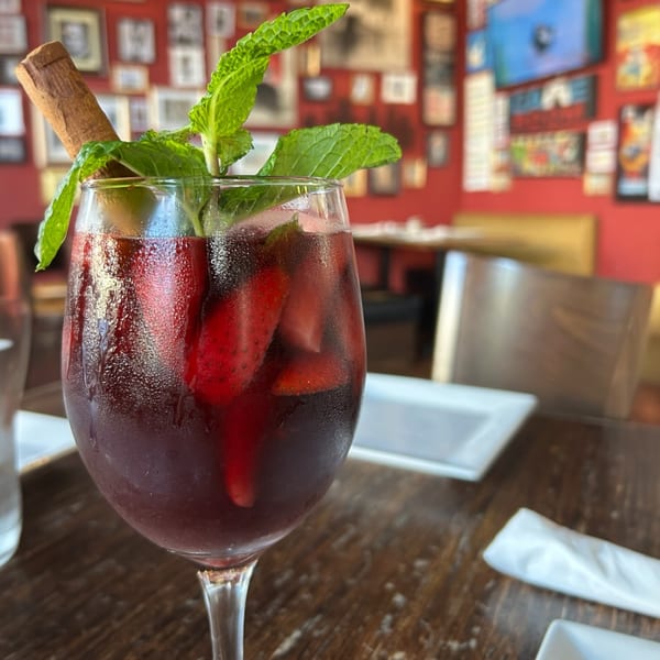 A glass of red sangria with strawberries, mint, and a cinnamon stick on a wooden table.