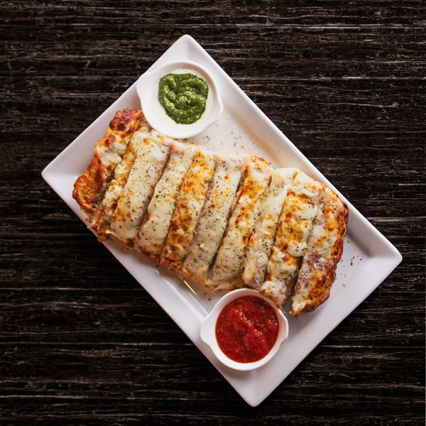 Cheesy garlic breadsticks with marinara and pesto dipping sauces on a white plate.