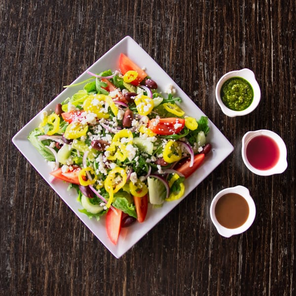 A fresh salad with tomatoes, peppers, olives, and feta cheese, served with three dressing options.