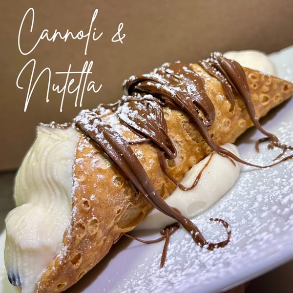 A cannoli filled with white cream, drizzled with Nutella, and dusted with powdered sugar.