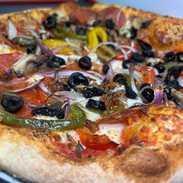 Close-up of a loaded pizza from UNCLE MIKE'S PIZZERIA with pepperoni, olives, peppers, and onions.