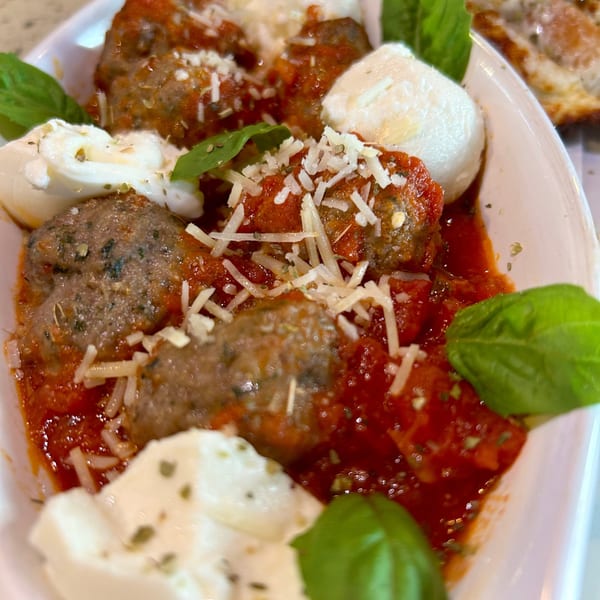 Meatballs in red sauce with fresh mozzarella, grated cheese, and basil in a white dish.