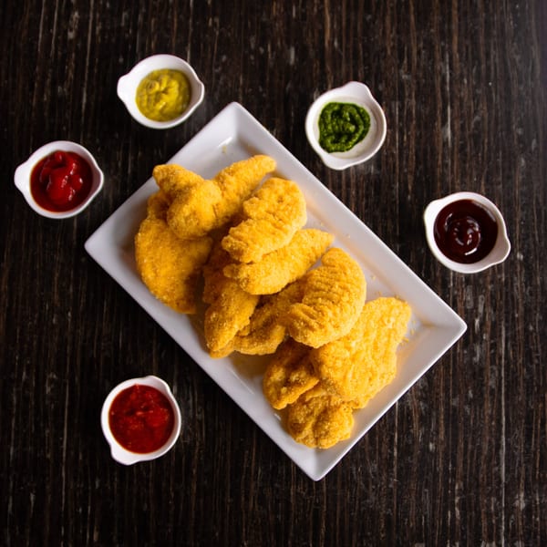 Golden chicken tenders on a white plate, surrounded by five small bowls of dipping sauces.